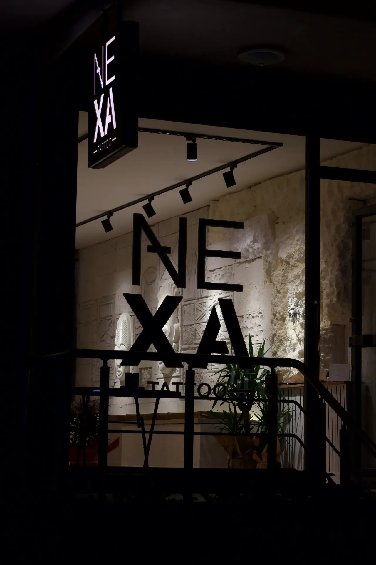 NEXA Atelier Küçükyalı dış cephesi: gece ışıklı NEXA tabelası ve taş duvarlı dövme stüdyosu girişi